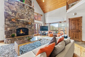 The great room boasts high ceilings, plenty of natural light, plush seating, and an impressive stone hearth fireplace.