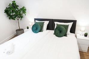 A cozy bedroom with a neatly made bed, green cushions, and a plant adding a touch of nature to the space.