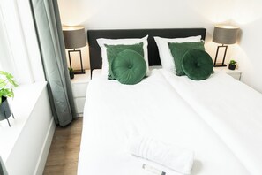 A cozy bedroom inside a stylish studio appartement Tilburg, featuring a neatly made bed with green cushions and modern bedside lamps. Perfect for Bed en Koffie near Tilburg Centrum – a warm and welcoming spot for University overnachten or Safaripark Beeksebergen overnachten. Comfort meets goedkoop living.