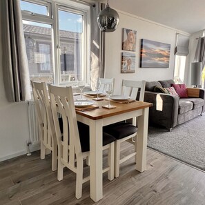 The open-plan dining area comfortably seats four guests and is adorned with placemats and coasters. Beyond the dining table, a cosy sofa and a heartwarming portrait of Willow create a welcoming atmosphere.