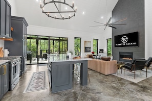 Open-concept floor plan invites the beauty of nature inside through expansive sliding glass doors & windows. The kitchen blends into the dining & living areas, all under soaring ceilings adorned with luxe fixtures, amenities, & furnishings.