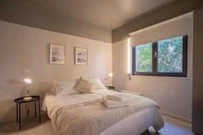 Relax in this serene bedroom with a cozy bed, soft lighting, and a refreshing view of lush greenery.
