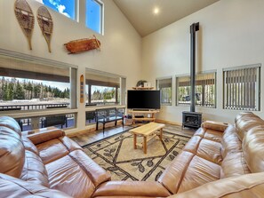 Living room featuring an electric fireplace, a 72" Smart TV, a luxurious leather sectional, a ceiling fan, and a stylish chandelier.