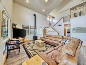 Living room featuring an electric fireplace, a 72" Smart TV, a luxurious leather sectional, a ceiling fan, and a stylish chandelier.