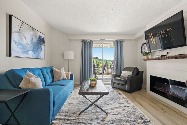 Living room with a smart TV, electric fireplace, cozy seating & access to the private patio.
