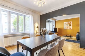 Bright and spacious dining area with an elegant chandelier and large windows, seamlessly connected to a cozy living space perfect for relaxation.