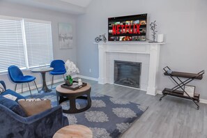 Enjoy the sleek comfort of our modern living area, complete with a cozy fireplace and a large flat-screen TV for your entertainment. The vibrant blue accents and contemporary design create an inviting space for relaxation and socializing.