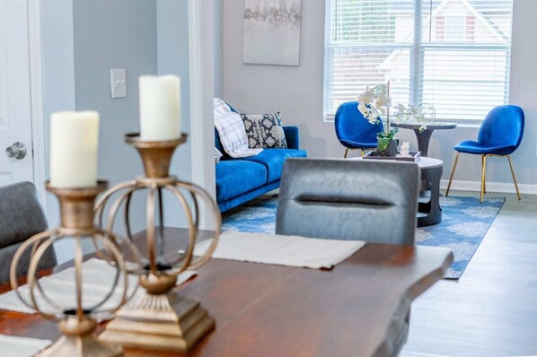 Experience the blend of comfort and style in our cozy retreat, featuring a vibrant blue sofa that adds a pop of color to the serene grey palette of the living space. Our space is designed for relaxation and conversation, with plush seating and ambient lighting to ensure a welcoming atmosphere. Perfect for those who appreciate modern aesthetics with a touch of warmth.