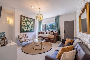 Step into our chic and cozy living space, where classic comfort meets modern elegance. Vibrant green drapes frame the large window, offering a view of the tranquil outdoors. Whether you're sipping morning coffee or enjoying evening cocktails, this beautifully curated space is designed for memorable moments.