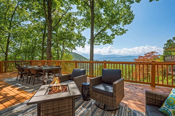 Unwind in the deck's lounging area with a central propane firepit and adjacent dining area, all while soaking in the magnificent mountain views