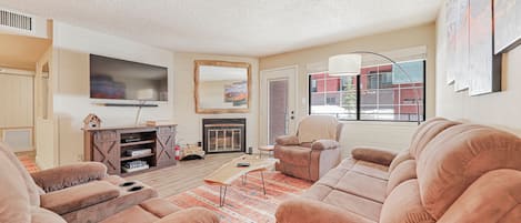 Cozy living space featuring a wood-burning fireplace, custom mirror, comfortable sofa and armchair, floor lamp, coffee table, media console, and a 53" smart TV—perfect for relaxing after a day in the mountains