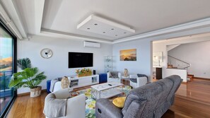Azure Serenity Villa's living room features a modern, large smart TV, AC, and abundant natural light, creating a bright and comfortable space for relaxation in Gaula, Santa Cruz Madeira. #moderndecor #luxury