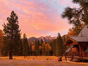 Experience the breathtaking beauty of a sunset at Peppermint Falls Ranch, where the sky transforms into a canvas of vibrant colors, casting a warm glow over the majestic view of The Needles and the Sugar Pine Lodge nestled among the trees.