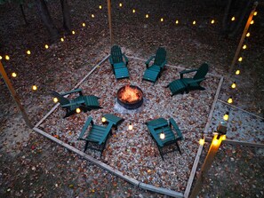 Cozy outdoor fire pit surrounded by wooden chairs and twinkling lights, perfect for stargazing and relaxation