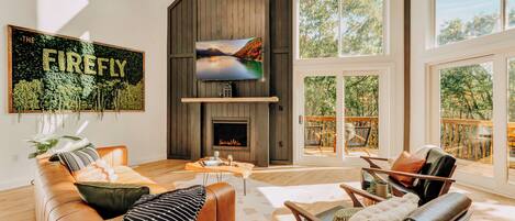 Primary Living room with large Smart TV and propane fireplace. Soak up the sun with gorgeous extra large A-frame windows. Learn more about our guest experience at truenorthpocono.com!