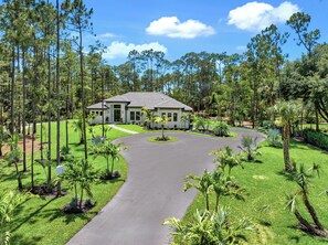 Welcome to your dream vacation home! This beautiful new construction home is nestled in a lush, private setting with a circular driveway, manicured landscaping, and surrounded by tall trees, offering a serene and inviting entrance.