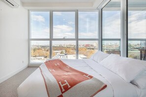 The second bedroom includes a queen bed, with floor-to-ceiling glazing offering views of the city. 