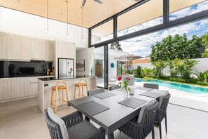 Open-plan living space with a sleek kitchen island, dining table with pool view, and high ceilings for a spacious feel