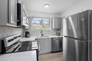 Kitchen equipped with refrigerator, four-place stove, microwave oven and cabinets.