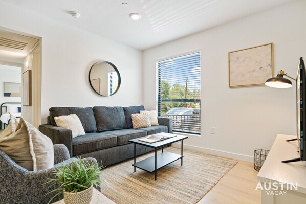 Bright living room with comfortable seating, smart tv, and queen sleeper with bedding