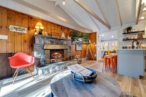 Cozy living room featuring a large-screen TV, AC, wood-burning fireplace, and a comfortable sectional sofa. Rustic charm with wood paneling creates the perfect atmosphere for relaxation