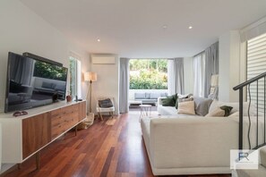 Living room with large luxurious couch, widescreen TV and doors opening to outdoor lounge area