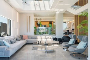 The living room features, a lush sofa,  a 65” TV and an advanced sound system