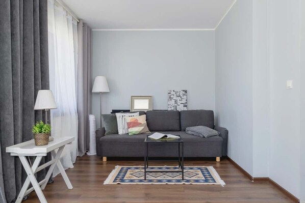 Bright, cosy living room with grey sofa bed and coffee table. Soft grey curtains and accessories set a homely atmosphere. 