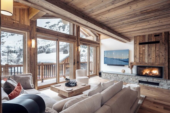 Relax in this spacious living room featuring a cozy fireplace, large windows with breathtaking mountain views, and comfortable seating perfect for unwinding after a day on the slopes.