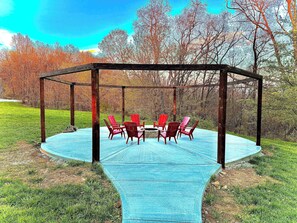 Spacious outdoor fire pit area with seating for the whole group. Relax under the open pergola, swap stories around the fire, and enjoy the peaceful wooded backdrop—perfect for big gatherings and unforgettable nights.