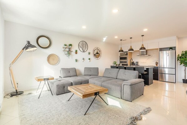 Spacious living area featuring a comfy grey couch and a wooden table—perfect for relaxing or entertaining.
