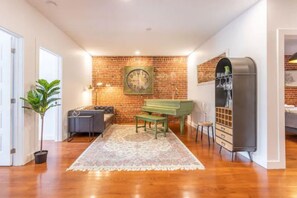 Entertainment area featuring white and brick walls, a piano, and a large stylish wall clock.