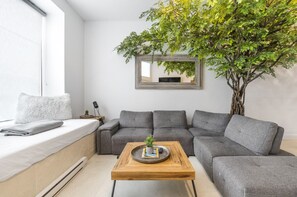Clean, minimalist white living area featuring a grey couch and wooden table for a modern, cozy vibe.