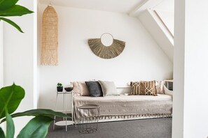 ozy interior featuring a beige daybed adorned with decorative pillows, complemented by neutral-toned side tables. Small decorative plants and accessories enhance the minimalist arrangement, creating an inviting and comfortable ambiance—perfect for a stylish and welcoming living space.