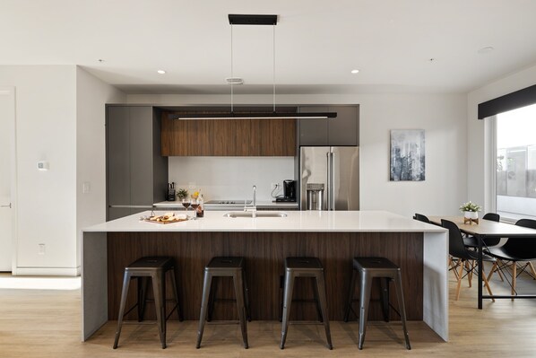 1st Floor: Fully equipped modern kitchen featuring culinary essentials, stainless steel appliances, island bar seating, and a dining area.