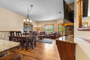 Main living area with dining table, sofa-bed, wall-mounted flatscreen TV, and private balcony.