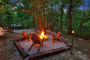 Escape to a serene woodland retreat featuring a cozy fire pit surrounded by Adirondack chairs. Relax under the trees with ambient lantern lighting, perfect for evenings spent outdoors. Ideal for unwinding in nature and enjoying peaceful nights by the fire.