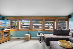 Living room with large windows offering stunning lake views, a comfortable sectional sofa, and a cozy TV setup—perfect for relaxing and enjoying the peaceful scenery.