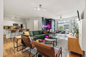 Enjoy a blend of modern comfort and style in this spacious living area. Featuring a plush sofa, chic decor, and a vibrant neon sign, it's perfect for relaxation and socializing. The open layout seamlessly connects to the kitchen and dining area.