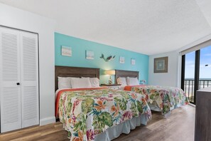 Drift off to sleep to the gentle ocean lull in the spacious ocean-view bedroom, featuring two queen beds, a smart TV, and balcony access.