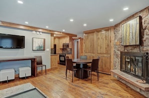 Elegant living and dining area with a large smart TV, comfortable seating, and a charming fireplace. The open layout allows for easy socializing and enjoying meals together in a stylish, wood-paneled setting.