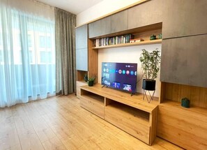 Spacious living room featuring an extensible sofa with decorative pillows, room darkening shades, multi-language library, plants, smart TV with Netfliix. and free Wi-Fi