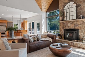 Cozy up in this inviting living room with a grand stone fireplace, vaulted ceilings, and large windows that frame stunning views of the surrounding nature. A perfect blend of warmth and elegance for your mountain retreat.