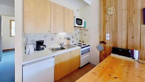The well-equipped kitchen features a four-burner stovetop, a microwave, a refrigerator, and a dishwasher, perfect for preparing meals after a day of exploring the mountains. The charming tiled backsplash adds a touch of rustic elegance to the space. A cof