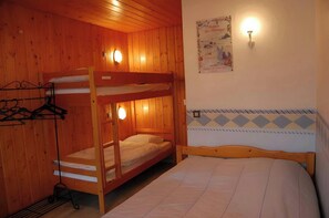 This cozy bedroom features a bunk bed with a single bed underneath, perfect for families or groups of friends. The room also includes a double bed with a white bedspread and a vintage poster on the wall, adding a touch of character to the space. The woode