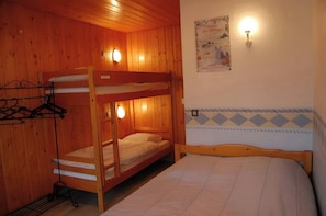 This cozy bedroom features a bunk bed with a single bed underneath, perfect for families or groups of friends. The room also includes a double bed with a white bedspread and a vintage poster on the wall, adding a touch of character to the space. The woode