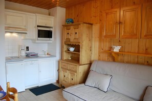 The cozy living area features a comfortable sofa bed, perfect for relaxing after a day on the slopes. The kitchenette is equipped with modern appliances, ensuring that you can prepare delicious meals during your stay. The wood-paneled walls and charming f