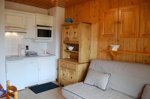 The cozy living area features a comfortable sofa bed, perfect for relaxing after a day on the slopes. The kitchenette is equipped with modern appliances, ensuring that you can prepare delicious meals during your stay. The wood-paneled walls and charming f