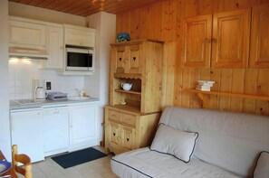 The cozy living area features a comfortable sofa bed, perfect for relaxing after a day on the slopes. The kitchenette is equipped with modern appliances, ensuring that you can prepare delicious meals during your stay. The wood-paneled walls and charming f