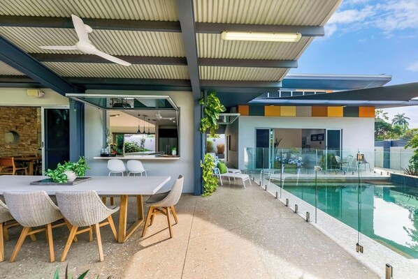 The undercover patio is a serene oasis with a servery from the kitchen, a large dining table and sun loungers facing the corner pool. 